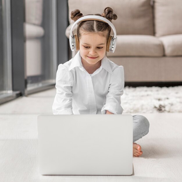 Little girl listening to her teacher through headphones at home