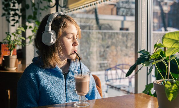 Little girl listens to music in headphones and drinks cocoa with sunny morning