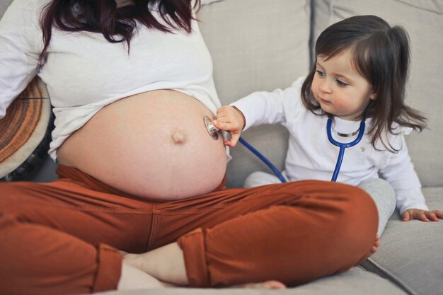 Little girl listens with a stethoscope in the belly of pregnant mom