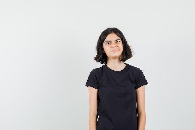 Little girl looking at front in black t-shirt and looking funny. front view.