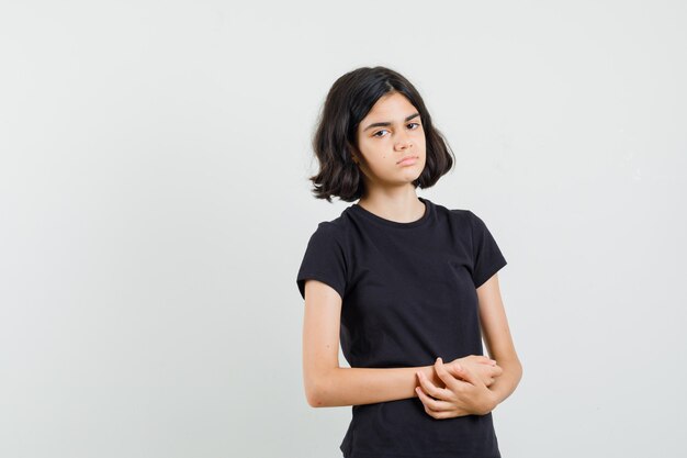 Little girl looking at front in black t-shirt and looking sad. front view.