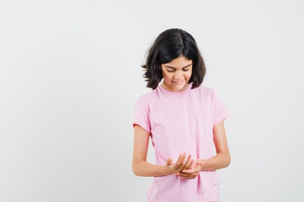 Little girl looking at her palms in pink t-shirt and looking jolly. front view.