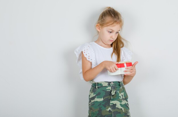 Little girl looking at present box in white t-shirt