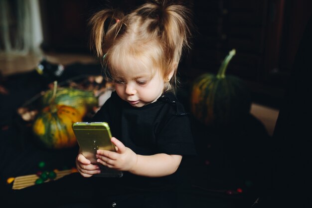 Маленькая девочка, глядя на смартфон с тыквенных фоне