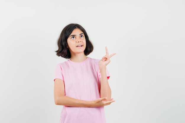 Little girl looking up, showing v-sign in pink t-shirt , front view.