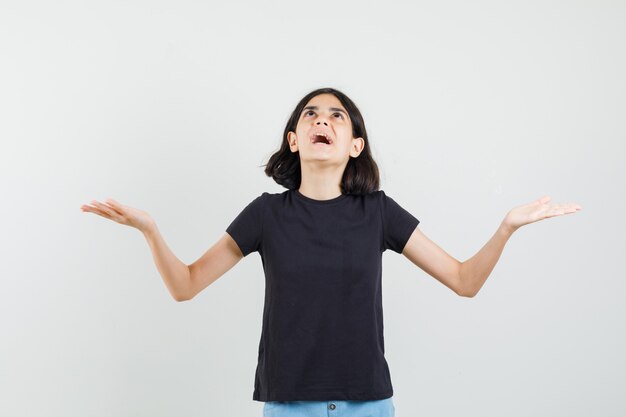 Little girl looking up, spreading arms in black t-shirt, shorts front view.