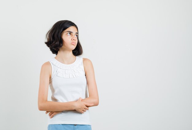 Little girl looking up in white blouse, shorts and looking concerned , front view.