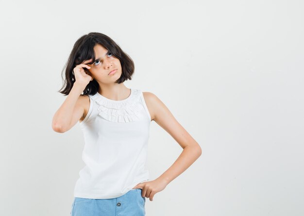 Little girl looking up in white blouse, shorts and looking pensive , front view.