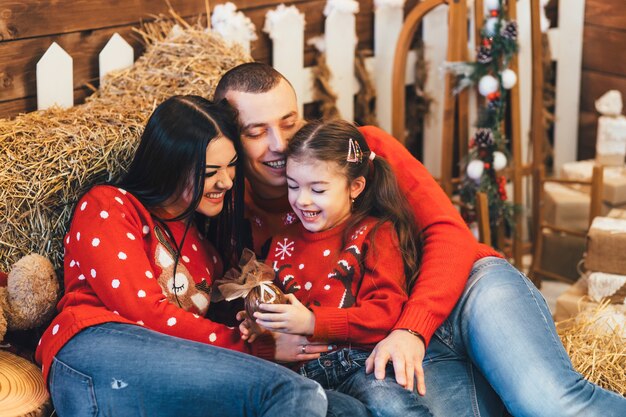 Little girl looks funny posing with her parents on the hay in a Christmas studio