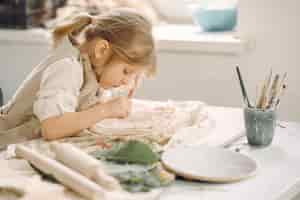 Бесплатное фото Маленькая девочка делает глиняную тарелку и украшает ее