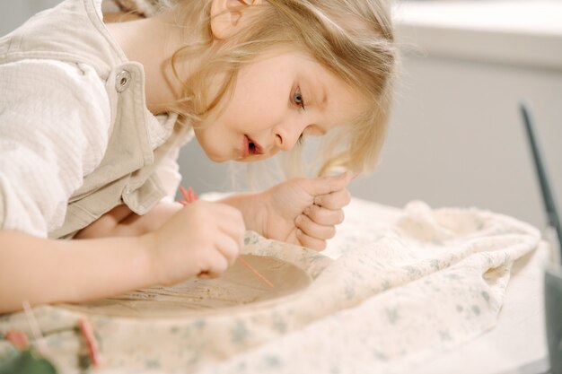 Little girl makes a clay plate and decorates it