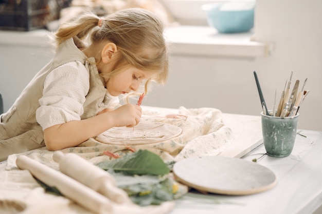 Маленькая девочка делает глиняную тарелку и украшает ее