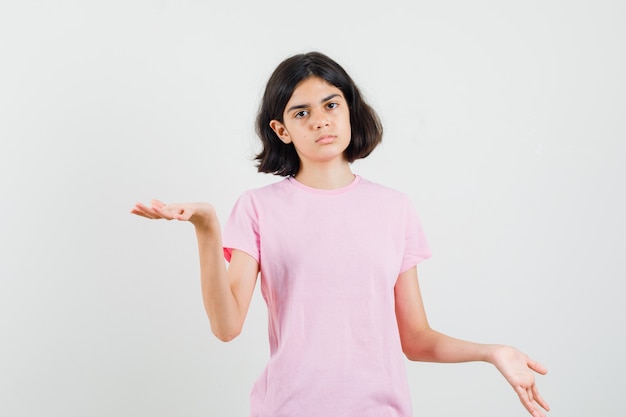 Little girl making scales gesture in pink t-shirt and looking serious. front view.