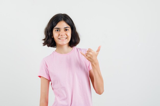 Little girl making shaka sign in pink t-shirt and looking glad , front view.