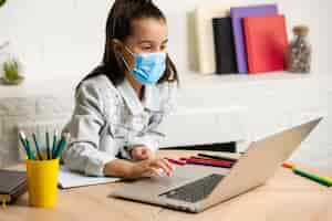 Free photo little girl in medical mask studying at home. epidemic, pandemic.