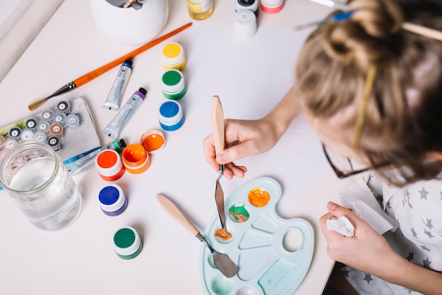 Little girl mixing gouache on palette at table