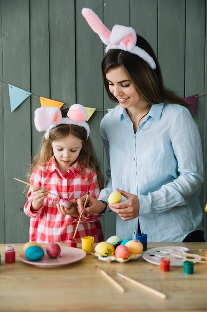 Little girl and mother in bunny ears painting eggs for Easter