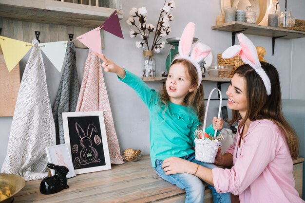 Little girl and mother in bunny ears sitting with basket of Easter eggs