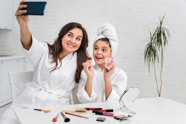 Little girl and mother taking a selfie while doing their make-up