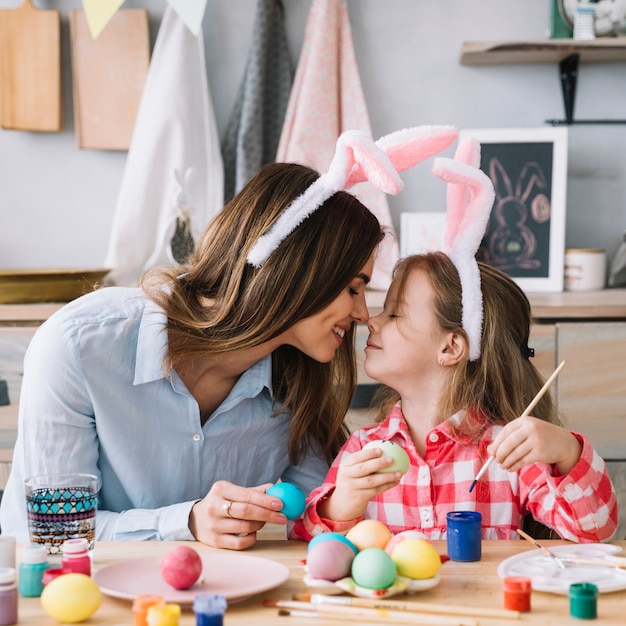 Little girl and mother touching noses while painting eggs for Easter
