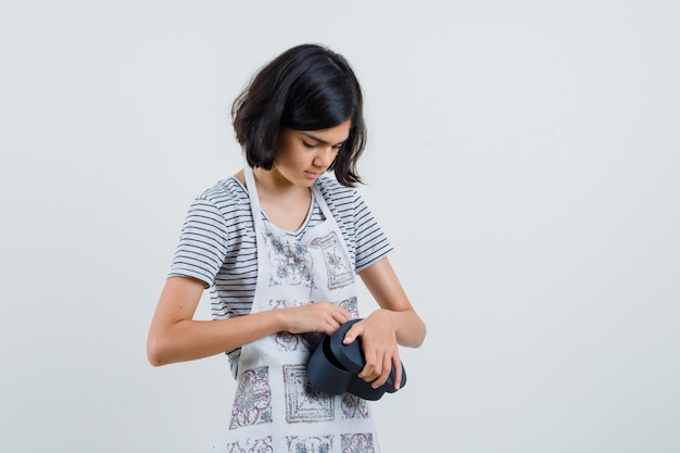 Little girl opening gift box in t-shirt, apron and looking curious.