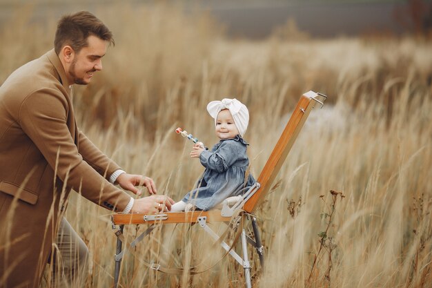 Little girl painting in a autumn field with father