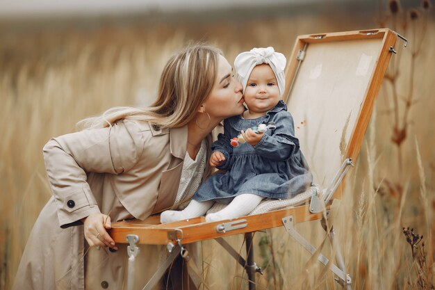 Little girl painting in a autumn field with mother