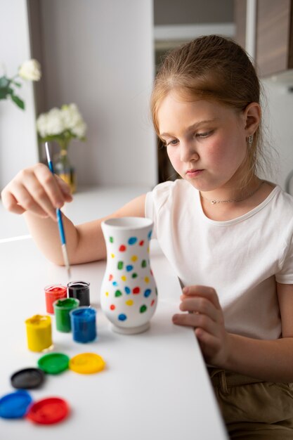 Little girl painting vase at home