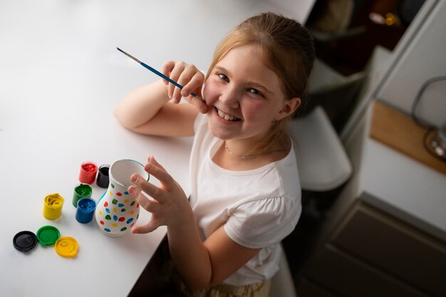 Little girl painting vase at home