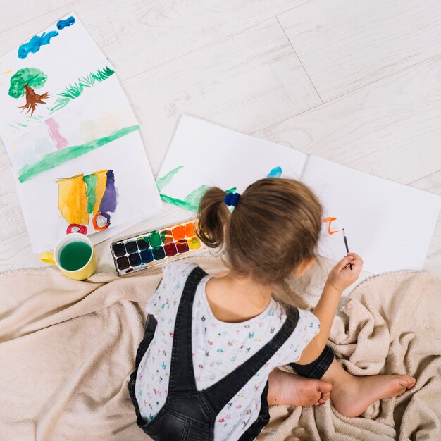 Little girl painting with aquarelle on floor