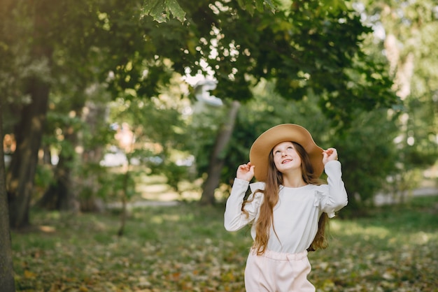 Маленькая девочка в парке стоит в парке в коричневой шляпе
