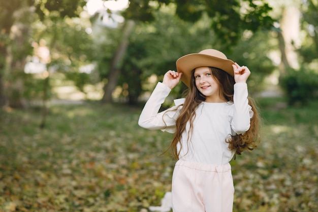 Маленькая девочка в парке стоит в парке в коричневой шляпе