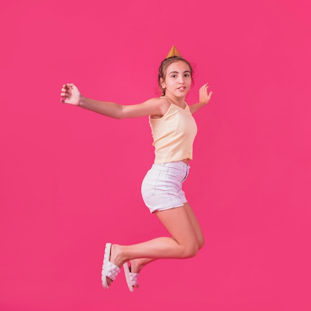Little girl in party hat jumping on pink backdrop