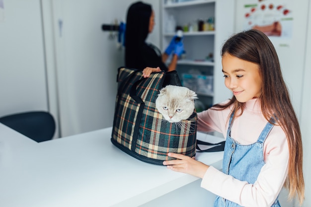 어린 소녀 애완 동물 주인은 산책을 위해 또는 동물 병원에서 특별한 케이지 캐리어에 고양이를 안고 있습니다