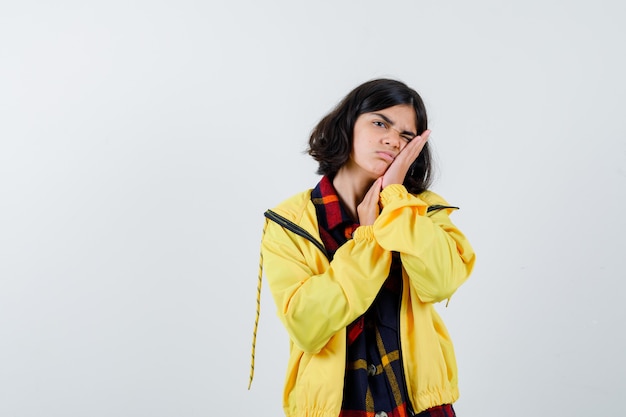 Little girl pillowing face on her hand in checked shirt, jacket and looking sleepy 