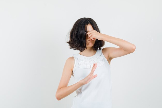 Little girl pinching nose due to bad smell in white blouse and looking disgusted , front view.