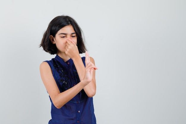 Little girl pinching nose and showing two fingers in blue blouse.