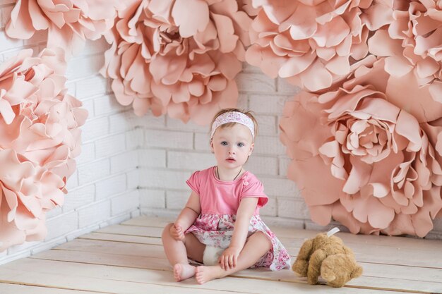 Маленькая девочка в розовом платье сидит среди больших розовых цветков бумаги