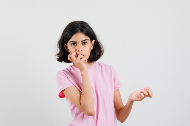 ピンクのTシャツを握りこぶしを噛み、物思いにふける、正面図の少女。