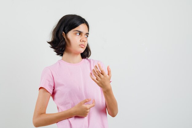 Little girl in pink t-shirt looking aside while gesturing with hands and looking dissatisfied , front view.