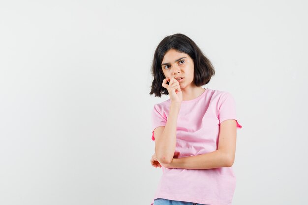 Little girl in pink t-shirt, shorts standing in thinking pose and looking worried , front view.