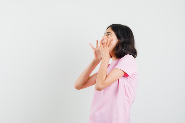 Bambina in maglietta rosa che grida con le mani vicino alla bocca.