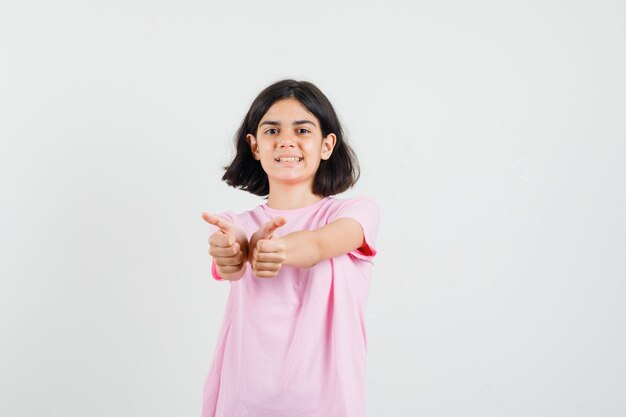 두 엄지 손가락을 표시 하 고 쾌활 한, 전면보기를 찾고 분홍색 티셔츠에 어린 소녀.