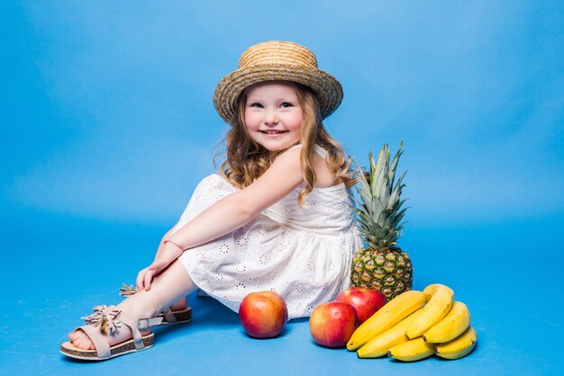 Little girl playing with fruits isolated on a blue wall