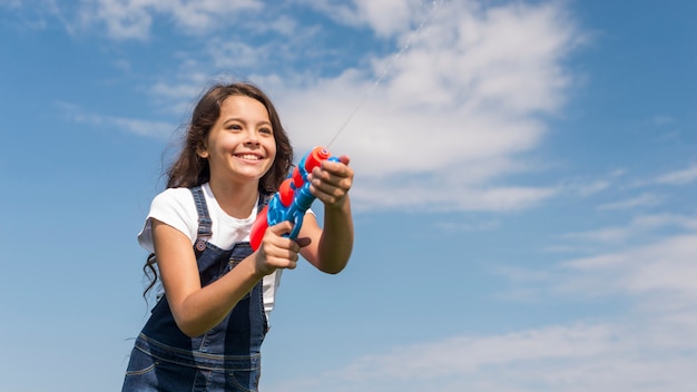 Бесплатное фото Маленькая девочка играет с водяной пушкой на улице