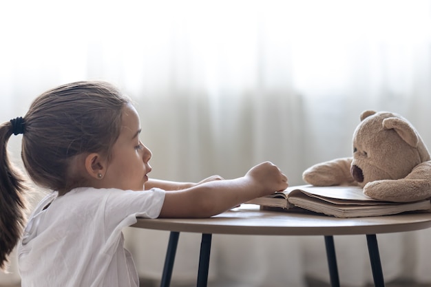 小さな女の子がテディベアと本で遊んだり、読書を教えたり、学校で遊んだりします。