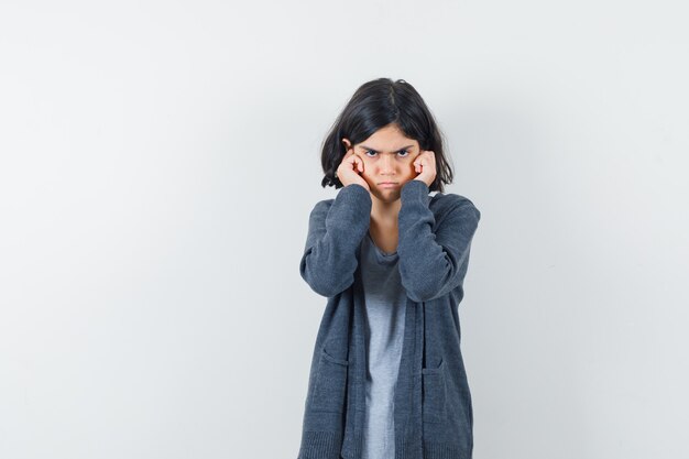 Little girl plugging ears with fingers in t-shirt, jacket and looking stubborn.