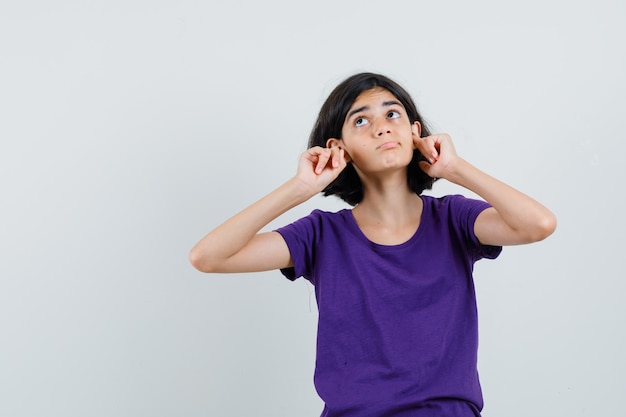 Little girl plugging ears with fingers in t-shirt and looking bored ,