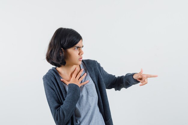 Little girl pointing aside in t-shirt, jacket and looking scared.