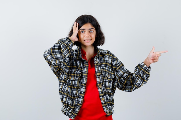 Little girl pointing aside while looking at camera in shirt,jacket and looking focused. front view.